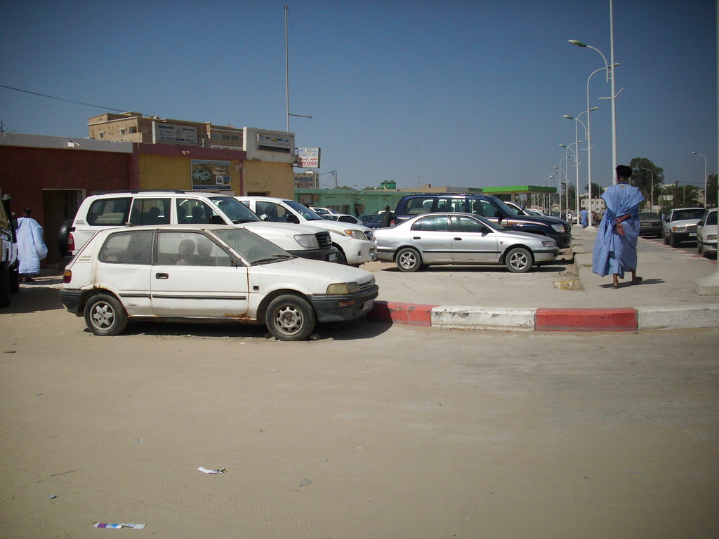 A buyer inspecting a used sedan on a dealership lot with a checklist in hand.