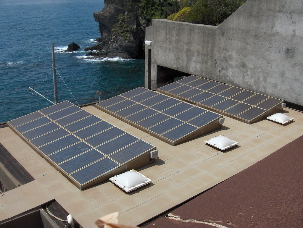 An installer placing solar panels on the roof of a single-family home on a sunny afternoon.